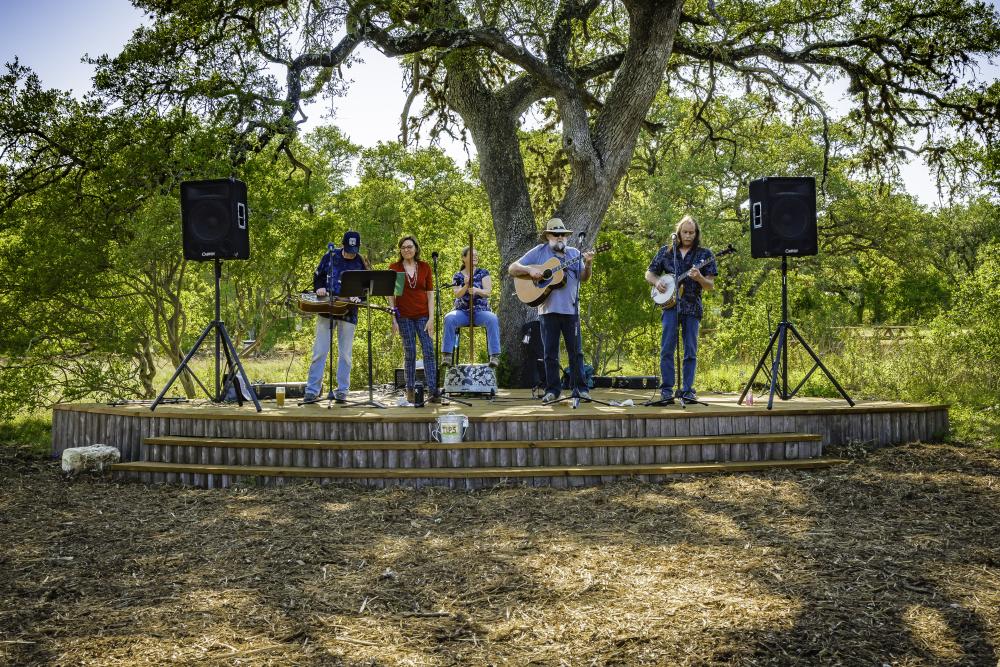 Five members of a bluegrass band play on the outdoor stage under a large tree at Vista Brewing