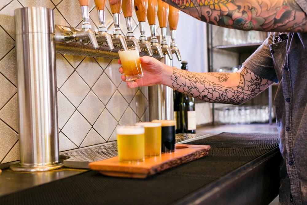 photo of person with tattooed arms pouring beer for a tasting flight at Vista Brewing in Austin Texas