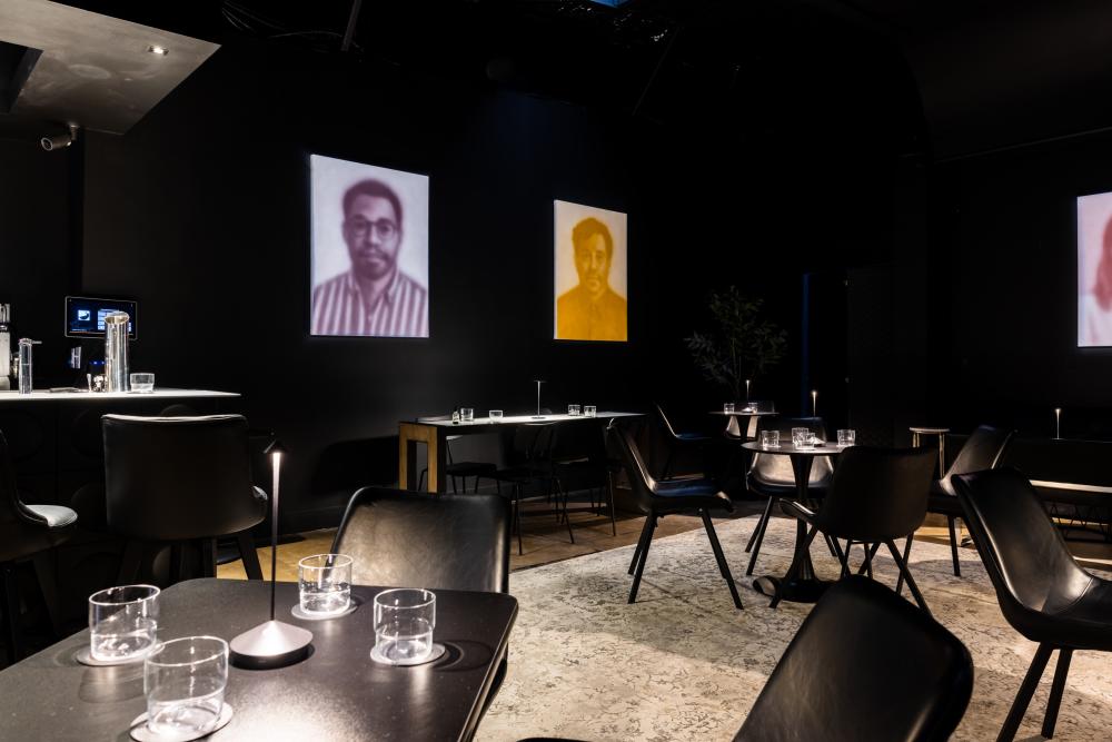 Art gallery/restaurant with blurry portraits on the wall and moody, dark seating.