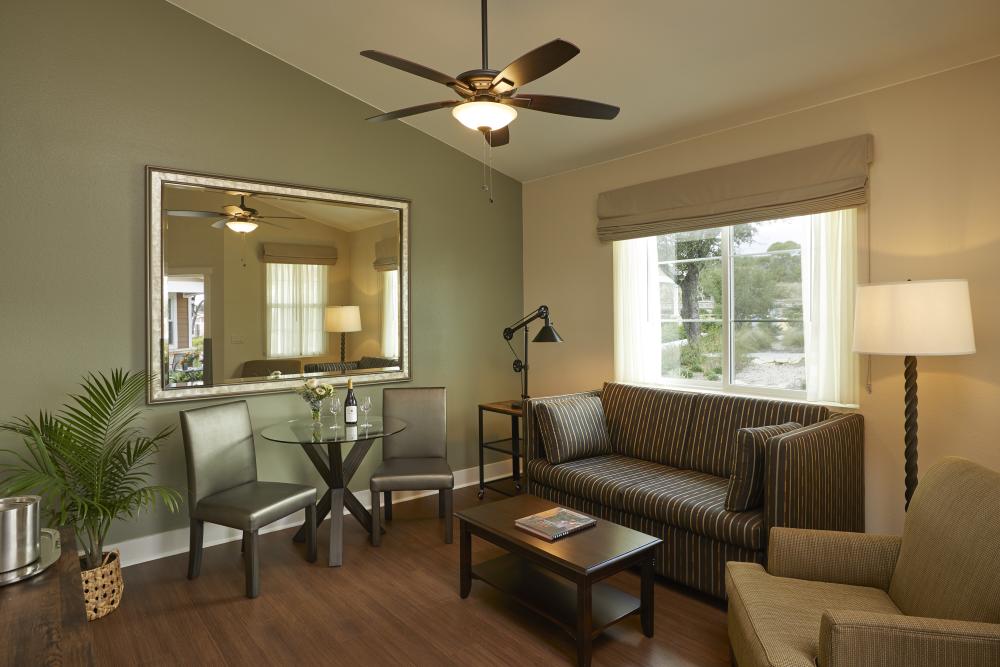 Photo of living area inside room at Carter Creek Winery with couch, chair, two lamos, small table and chairs, window and mirror on the wall