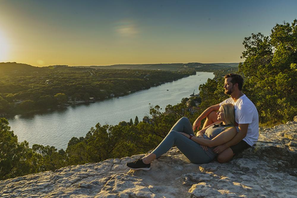 Couple lounging atop Mount Bonnell at sunset, overlooking Lake Austin
