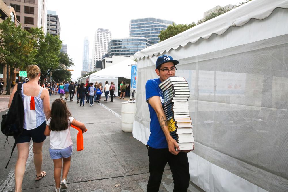 Teen carries a stack of books at the Texas Book Festival in Austin Texas