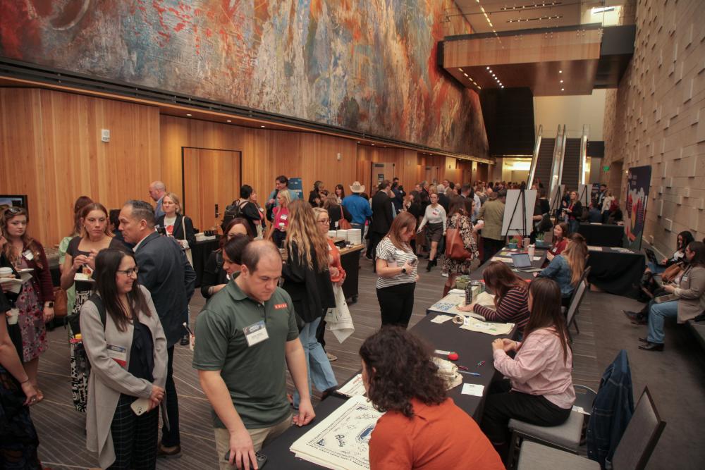 Conference attendees in a prefunction space getting badges, interacting with vendors and having conversations with eachoter.