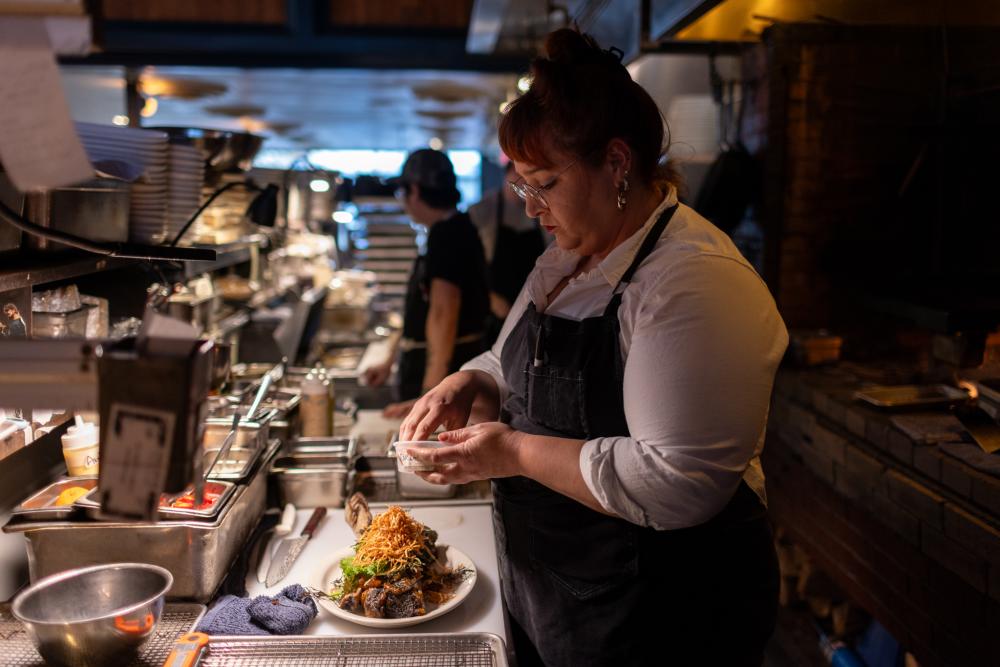 Chef in Dai Due kitchen topping a giant beef rib with crispy fried onion strings.