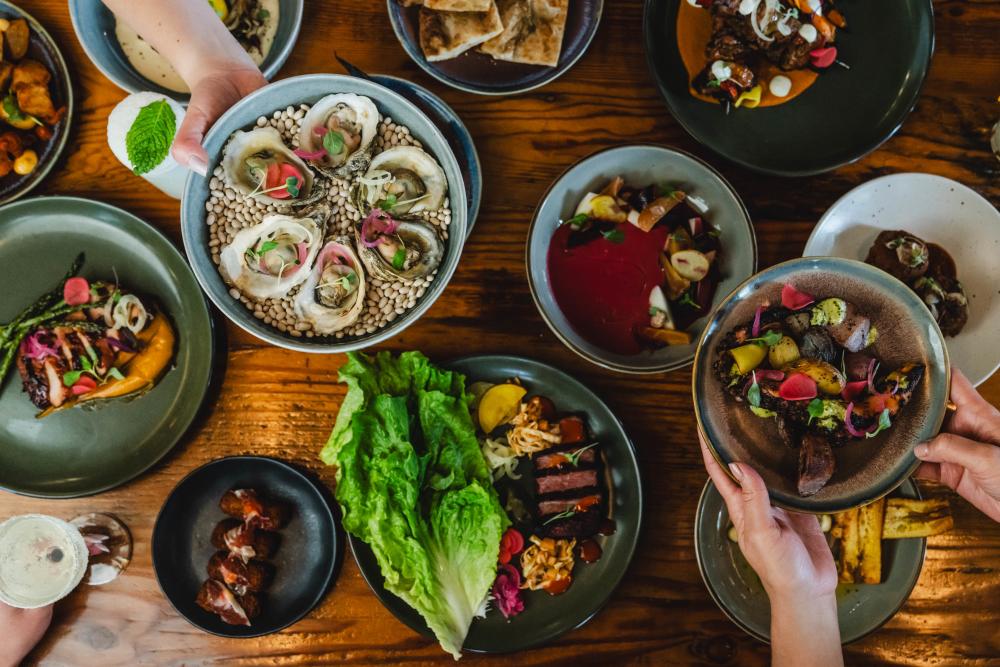 Various plates of colorful tapas with two people reaching plates into the frame.