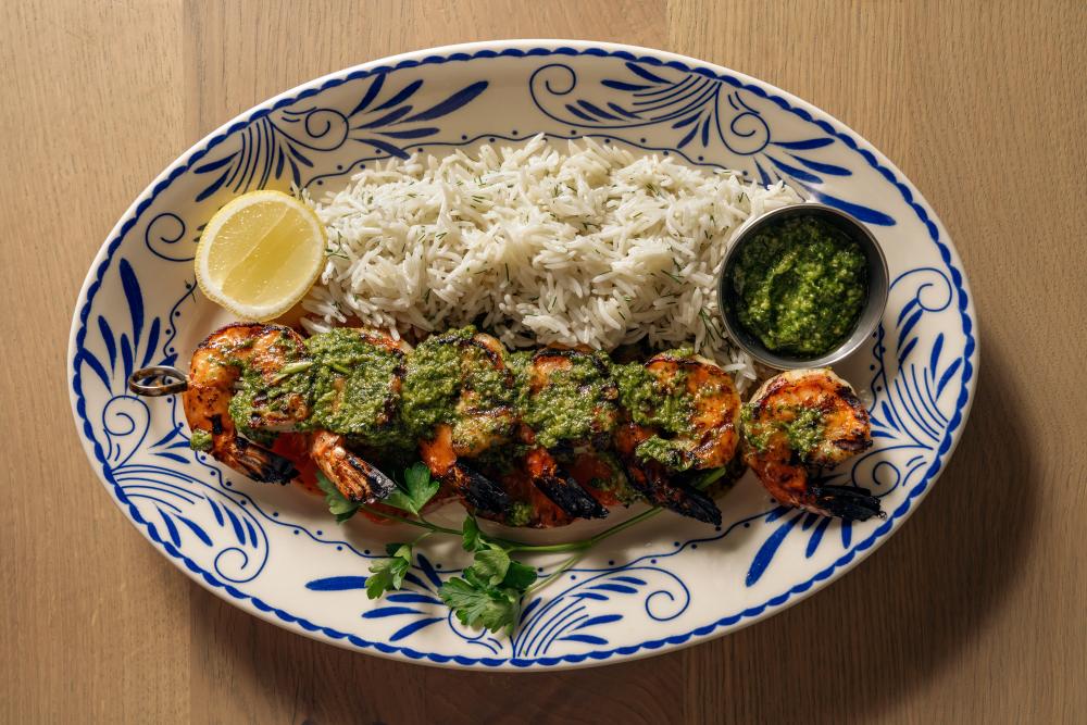 A shrimp skewer with green herb sauce on top served with white rice on a blue dish at Ema.