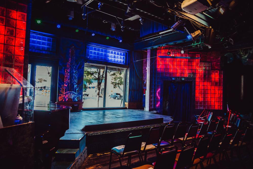 Empty stage at Esther's Follies. There are windows behind the stage and red lights on surrounding walls