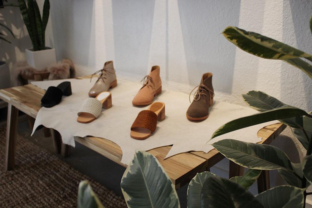 Line up of Chelsea Boot and espadrille-style shoes on a wooden table, surrounded by plants.