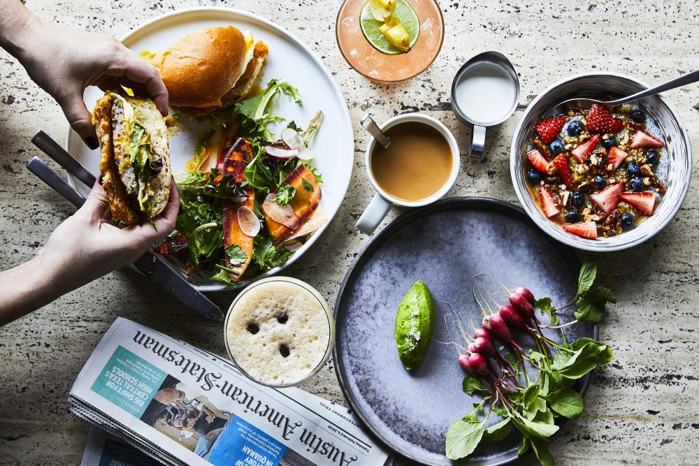 Brunch spread including a coffee, breakfast sandwich, yogurt parfait and veggie plate.