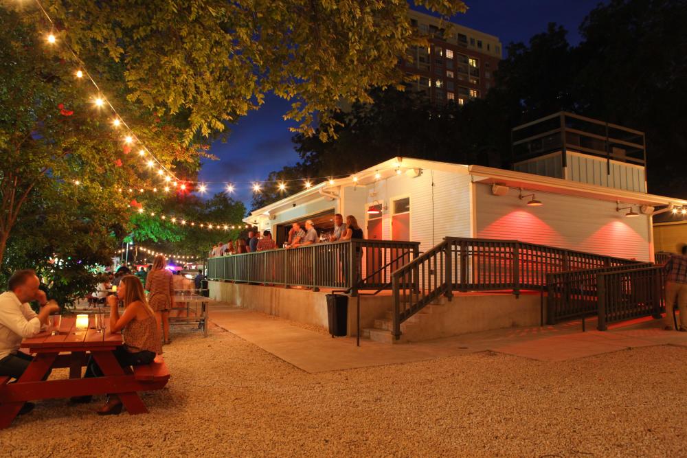 Illuminated string lights hanging over people drinking cocktails on Half Step Bar's back patio.