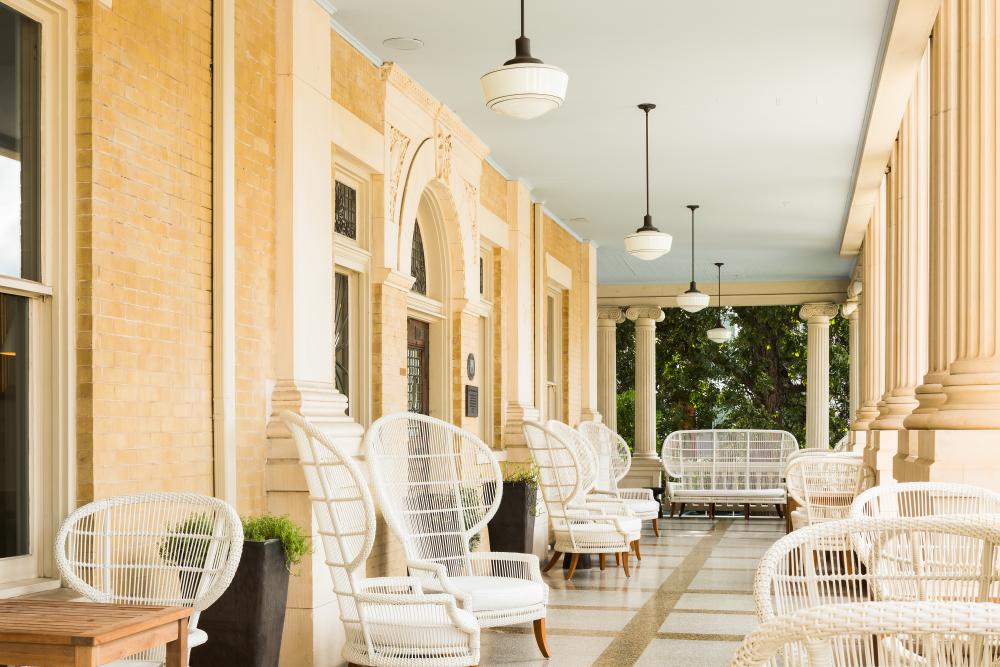 Hotel Ella covered patio alongside the building. Empty white chairs and settees are placed throughout the space