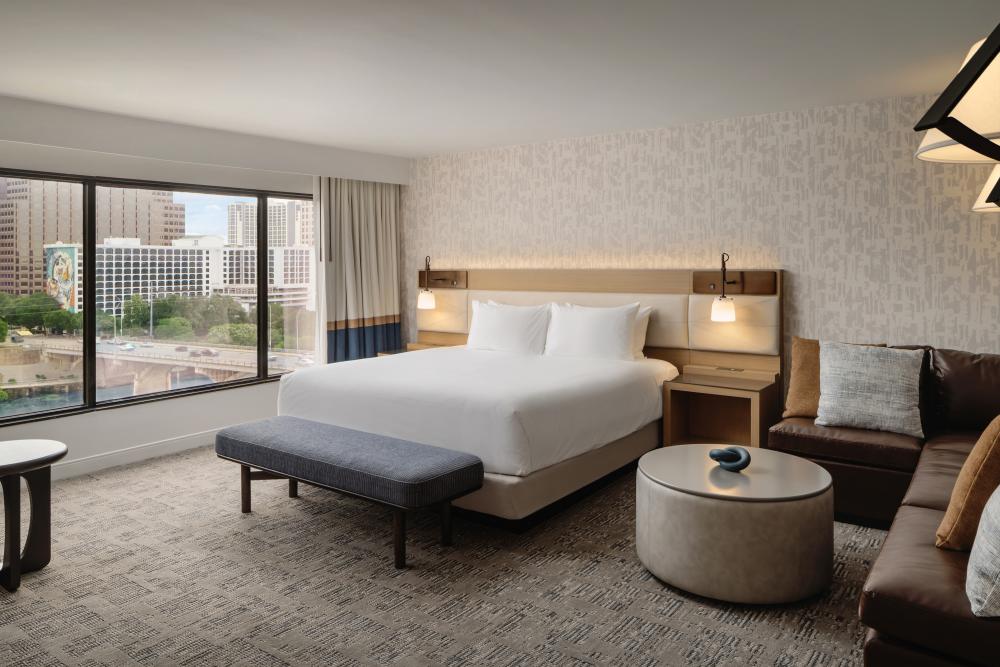 Modern and spacious hotel room with bed, couch and coffee table and large windows overlooking the Congress Avenue Bridge and Lady Bird Lake.