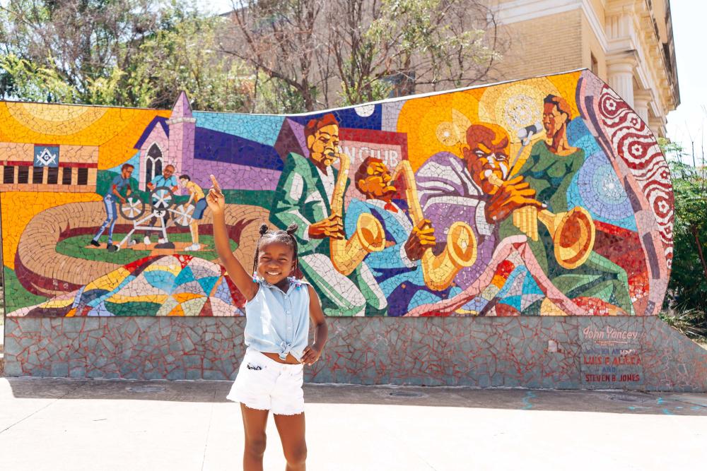 Child strikes a pose in front of the Rhapsody mosaic in East Austin depicting Austin's Black musical heritage