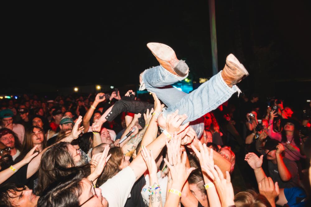 Man crowdsurfing while singing into a microphone while a crowd cheers and smiles.
