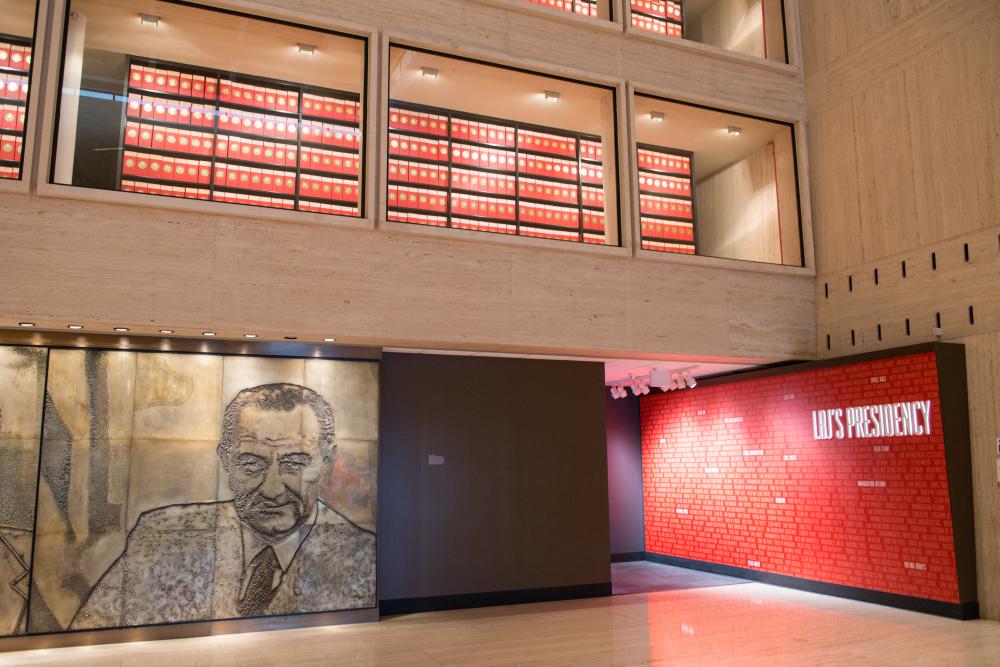 Interior atrium of the LBJ Presidential Library, showcasing archives, a stone mural of President LBJ and a preview of the hallway exhibit that outlines his presidential legacy.
