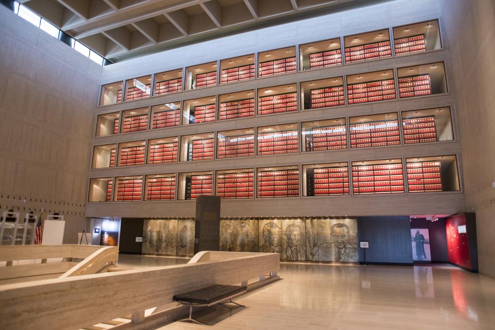 View from the top of the stairs at the LBJ Presidential Library and Museum, looking at rows of red books and accolades in the great hall.