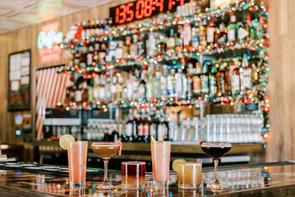 Image of several different style cocktails sitting on the bar with festive colorful lights in the background at Lala's Little Nugget South.