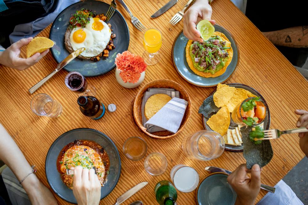 Lay flat image of multiple dishes sitting on the table with people eating around the table at La Condesa.