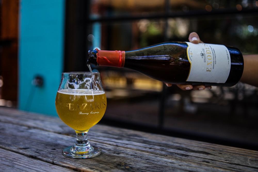 Photo of hand pouring a bottle of beer labele Exodus into tulip glass labeled Lazarus Brewing Company