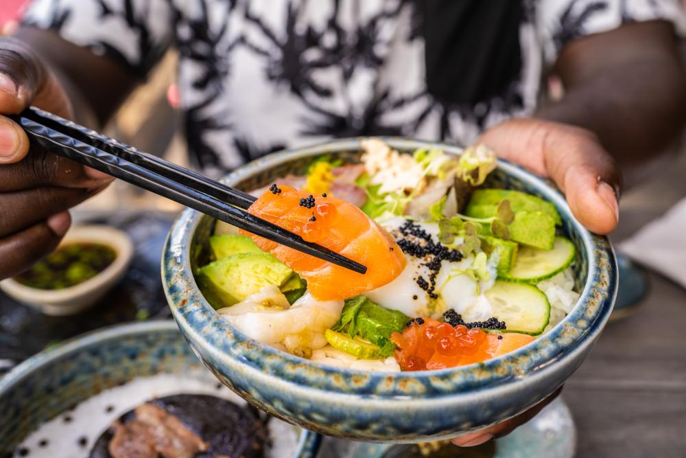 A man holds a piece of fish with chopsticks, over a colorful dish at Lucky Robot