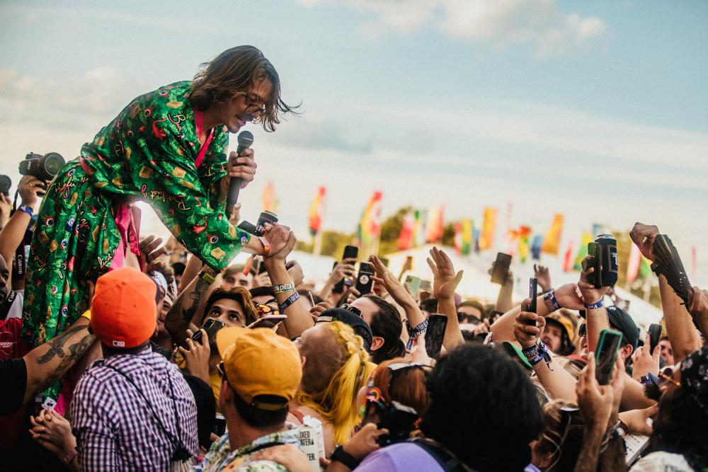 Musician reaching into crowd of people surrounding a stage.