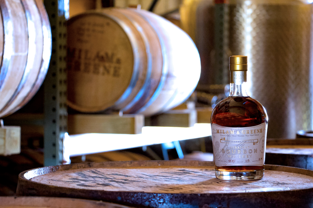 Bottle of Milam and Greene whiskey on whiskey barrel in rack room.