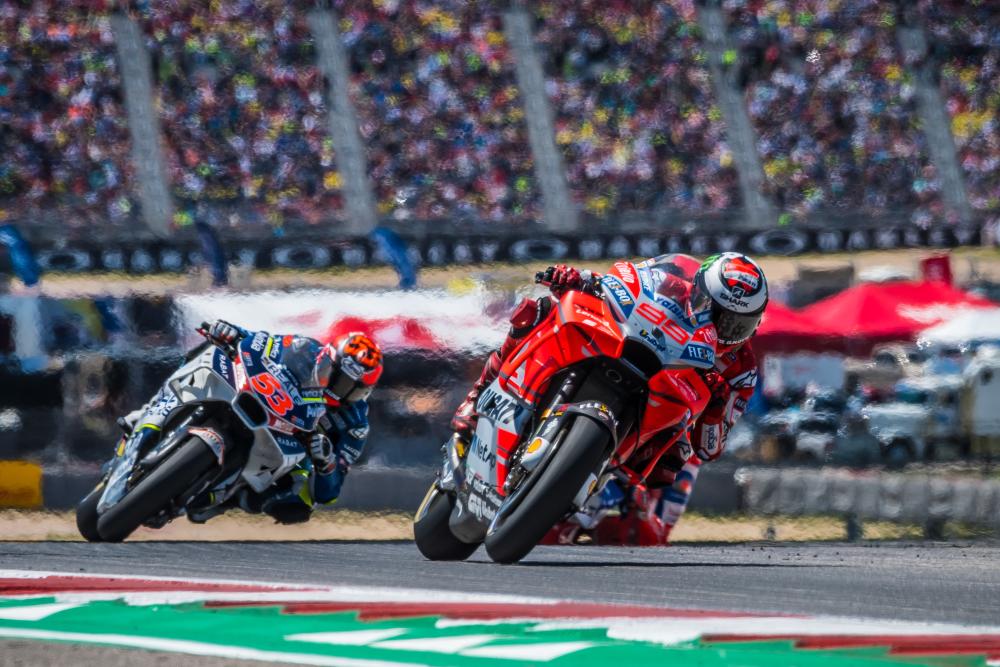 People on motorcycles zooming around a corner at the COTA track.