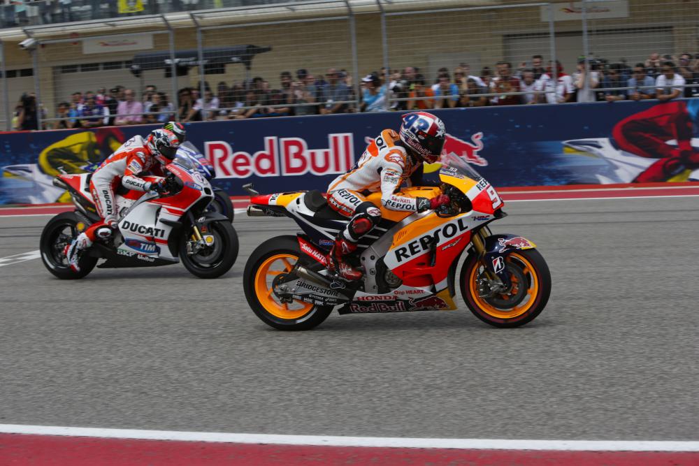 Two people on motorcycles, moving past a crowd of people.