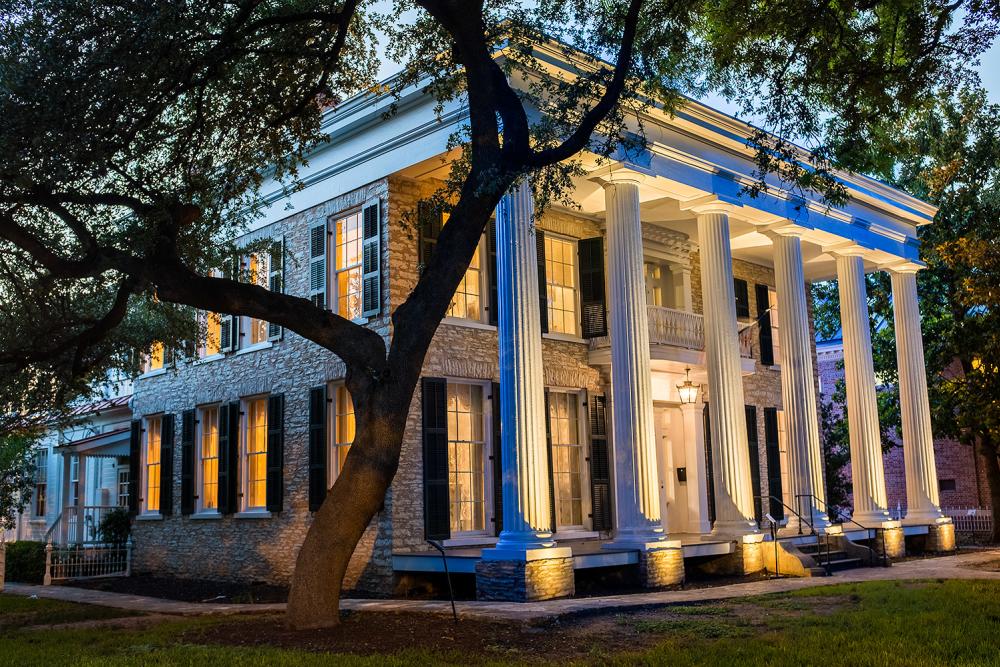 A yellow glow shines out through the windows and illuminate the Greek-style columns of the Neill-Cochran House Museum at twilight