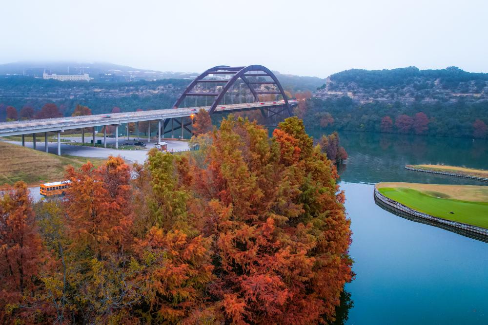 View of Lake Austin lined with fall-colored trees and the Penny Backer Bridge against a foggy Hill Country.
