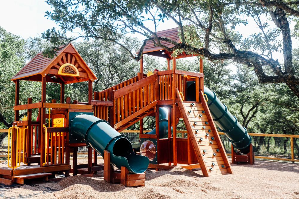 Photo of a large wooden playground at Family Business Beer Co with three plastic slides and a small rock climbing area