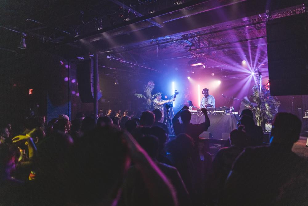 DJ spinning on neon lit Empire Control Room stage with crowd of people raising their hands in the air.