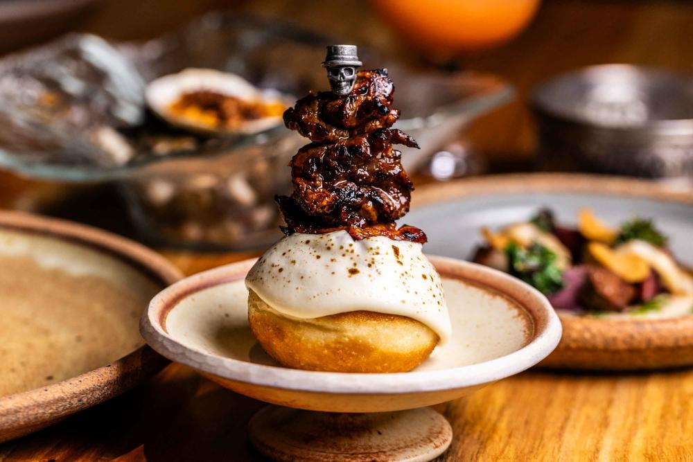 Small, round pastry topped with cream and a skull-topped skewer covered in crispy bacon.