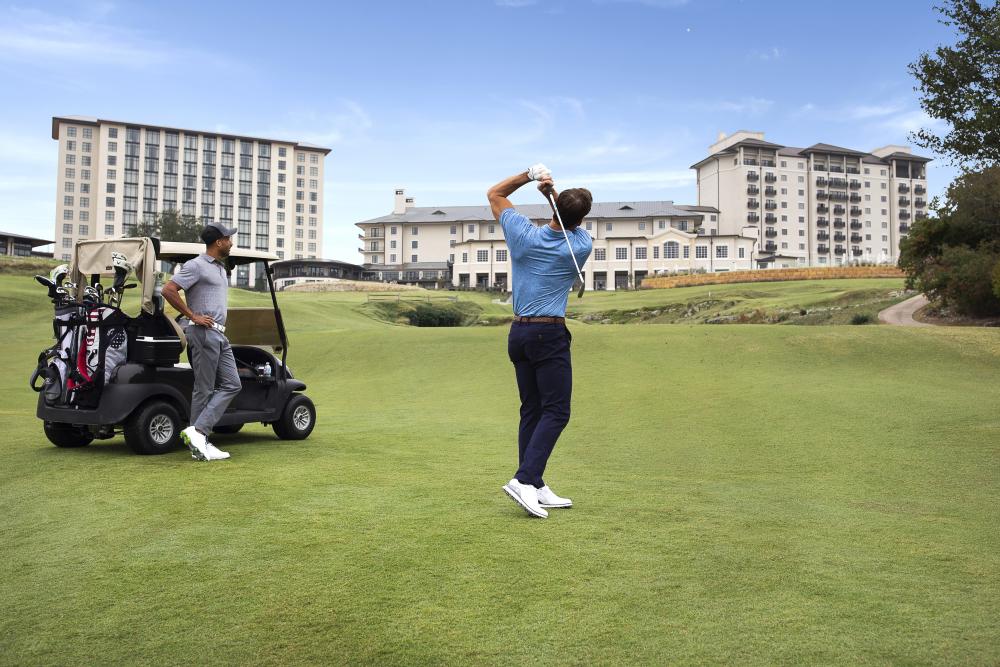 One man plays golf while another leans up against a golf cart at the Fazio Foothills course at Barton Creek Resort & Spa