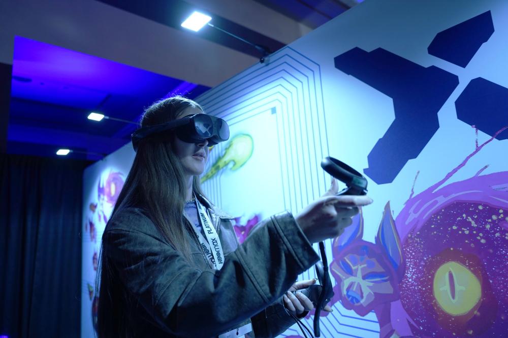 Woman using VR headset and controllers in a conference exhibit booth.
