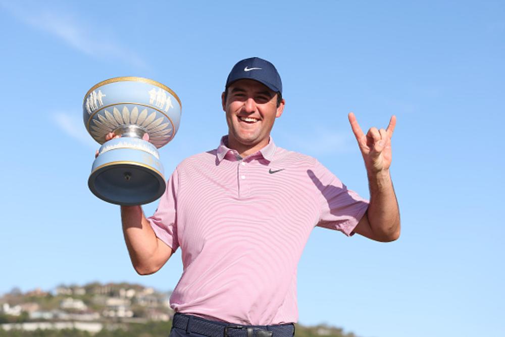 Scottie Scheffler holding up "hook 'em horns" hand sign with trophy in hand.