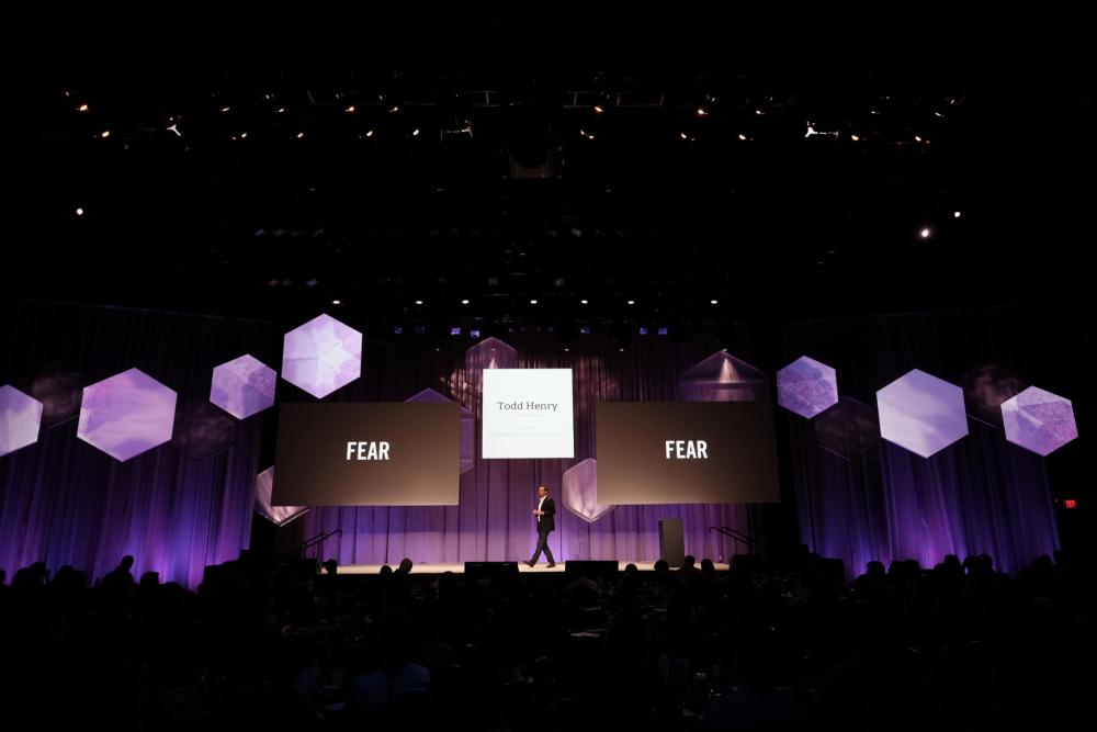 Todd Henry stands on stage at ACL Live at the Moody Theater with three screens behind him, during a presentation at Spredfast