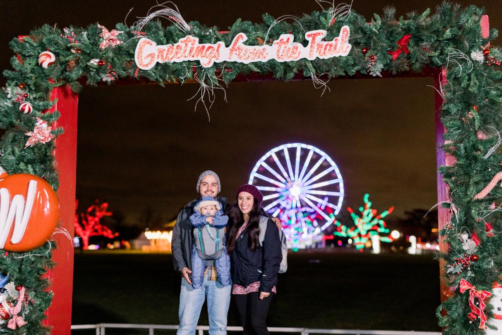 Parents and baby standing under photo opp frame at Austin Trail of Lights