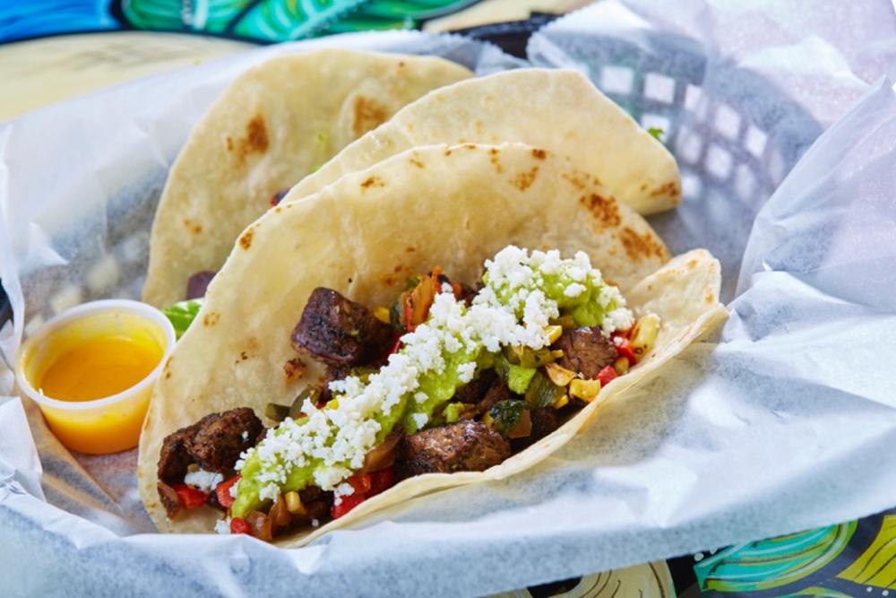 Two Tacodeli tacos filled with dry-rubbed beef tenderloin, grilled corn, caramelized onion, roasted peppers, guacamole and queso fresco.