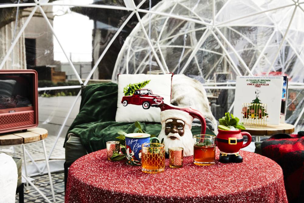 Cute holiday set up with lounge furniture, record player, holiday-themed cups and drinks inside of a pop up igloo.