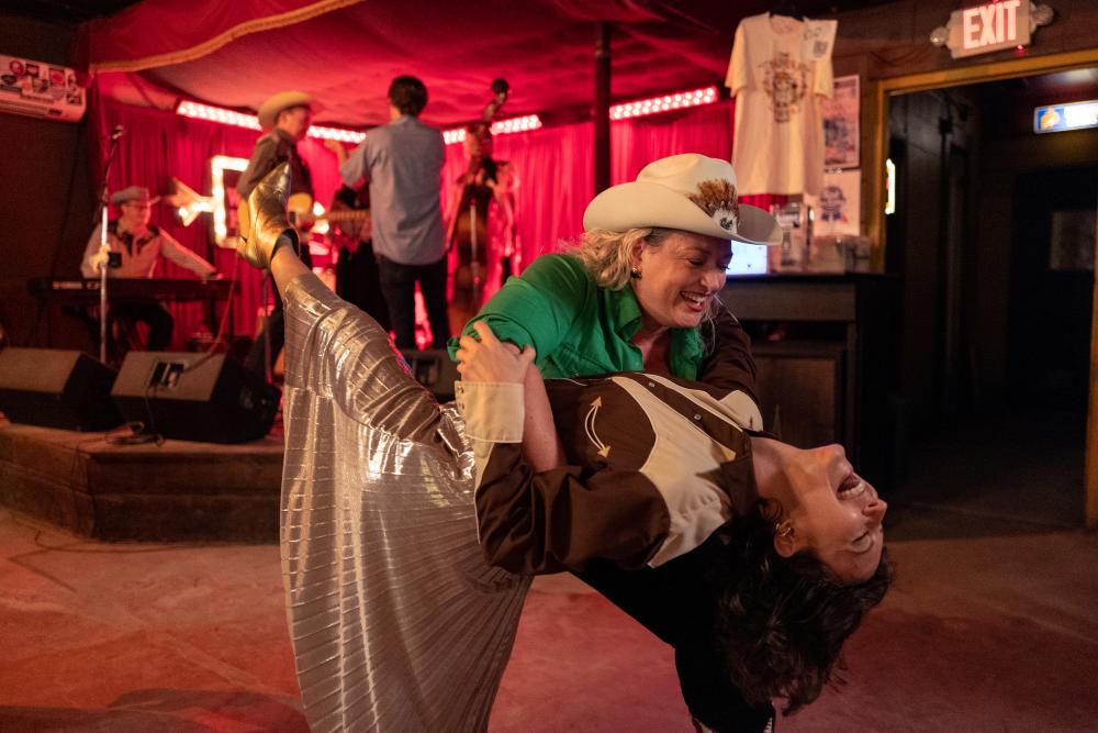 Two women in Western attire country dancing in a dance hall.