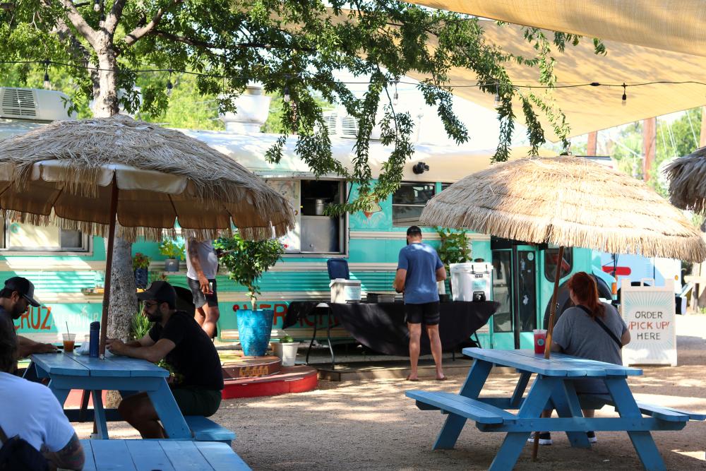 Veracruz All Natural food truck with people sitting at grass umbrella-shaded picnic tables.