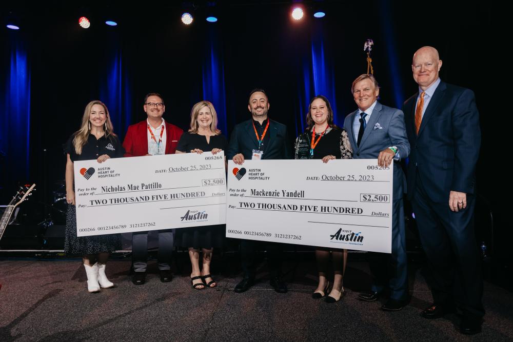 Two women and two men on a stage holding a giant check for scholarship recipient.