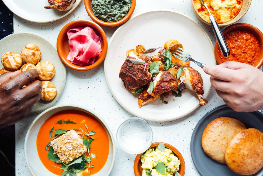 Two hands reaching over colorful plates of roast chicken, fish and savory sides.
