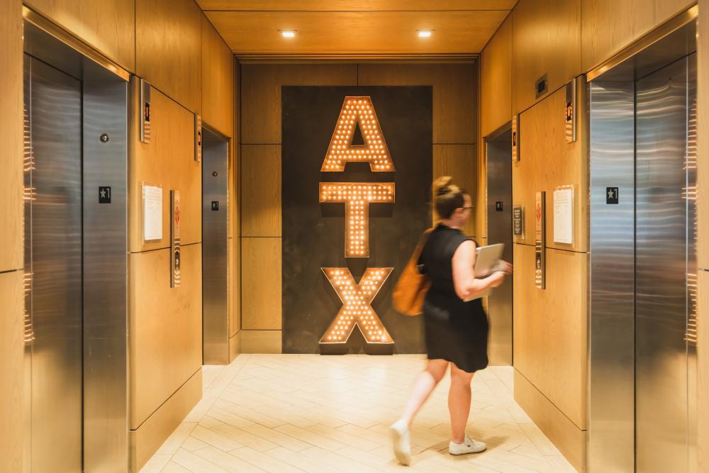 Woman walking into an elevator, passing by a large ATX sign in an elevator atrium.