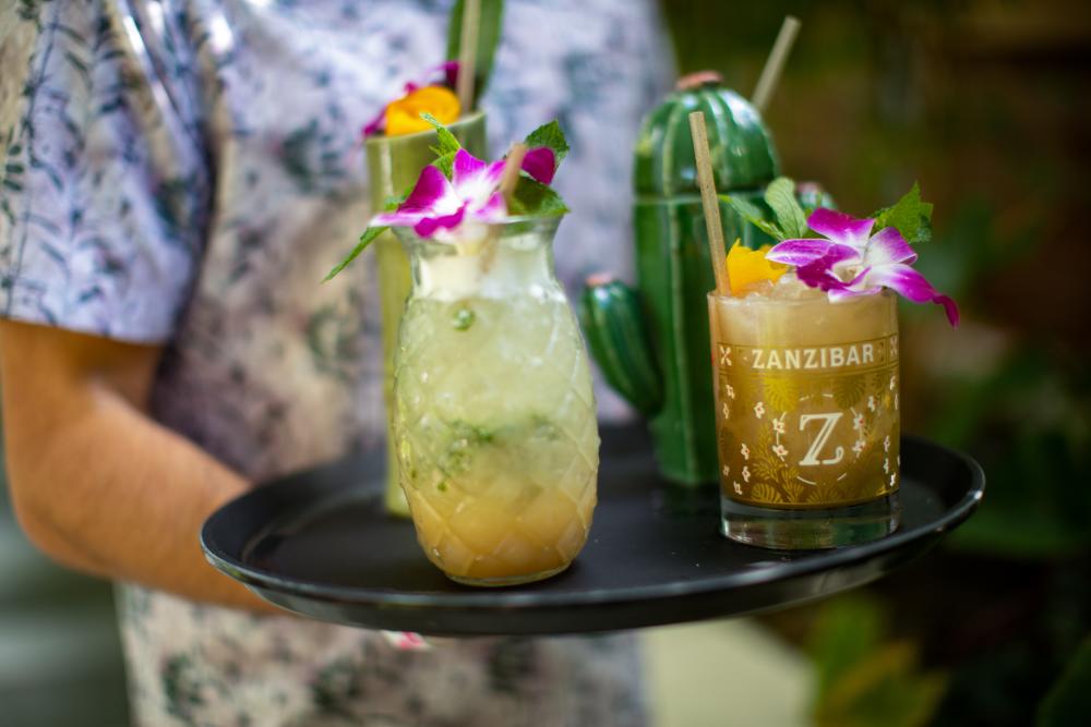 A waiter carries four different tiki cocktails on a tray at Zanzibar in Austin Texas