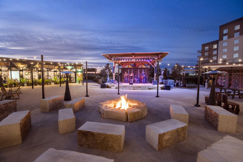 Stone seats surrounding a fire pit at Kalahari Resort's Amatuli. Photo is outdoors at twilight and a band is playing on stage in the background