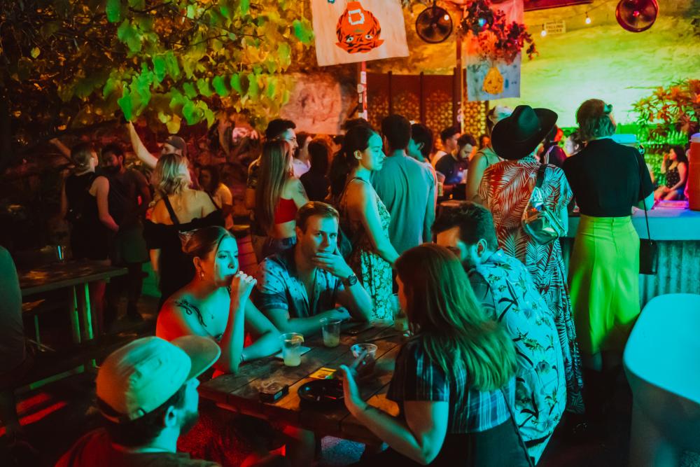 Crowd of people near a bar under blue and lime colored lights.