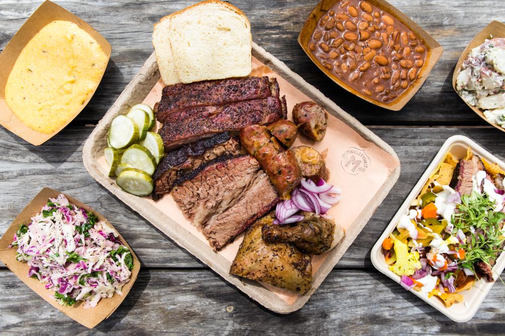 Overhead view of a platter of bbq meats and sides like beans, slaw, grits and potato salad