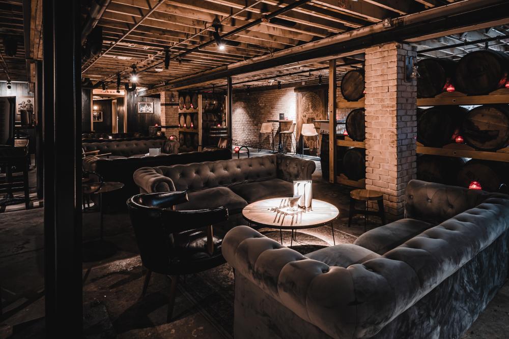 Interior of DuMonts Down Low basement bar with dark couches and whiskey barrels in Austin Texas